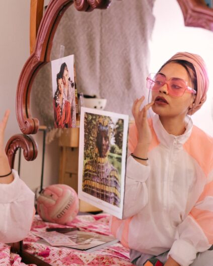 trendy ethnic woman applying lip balm in front of mirror