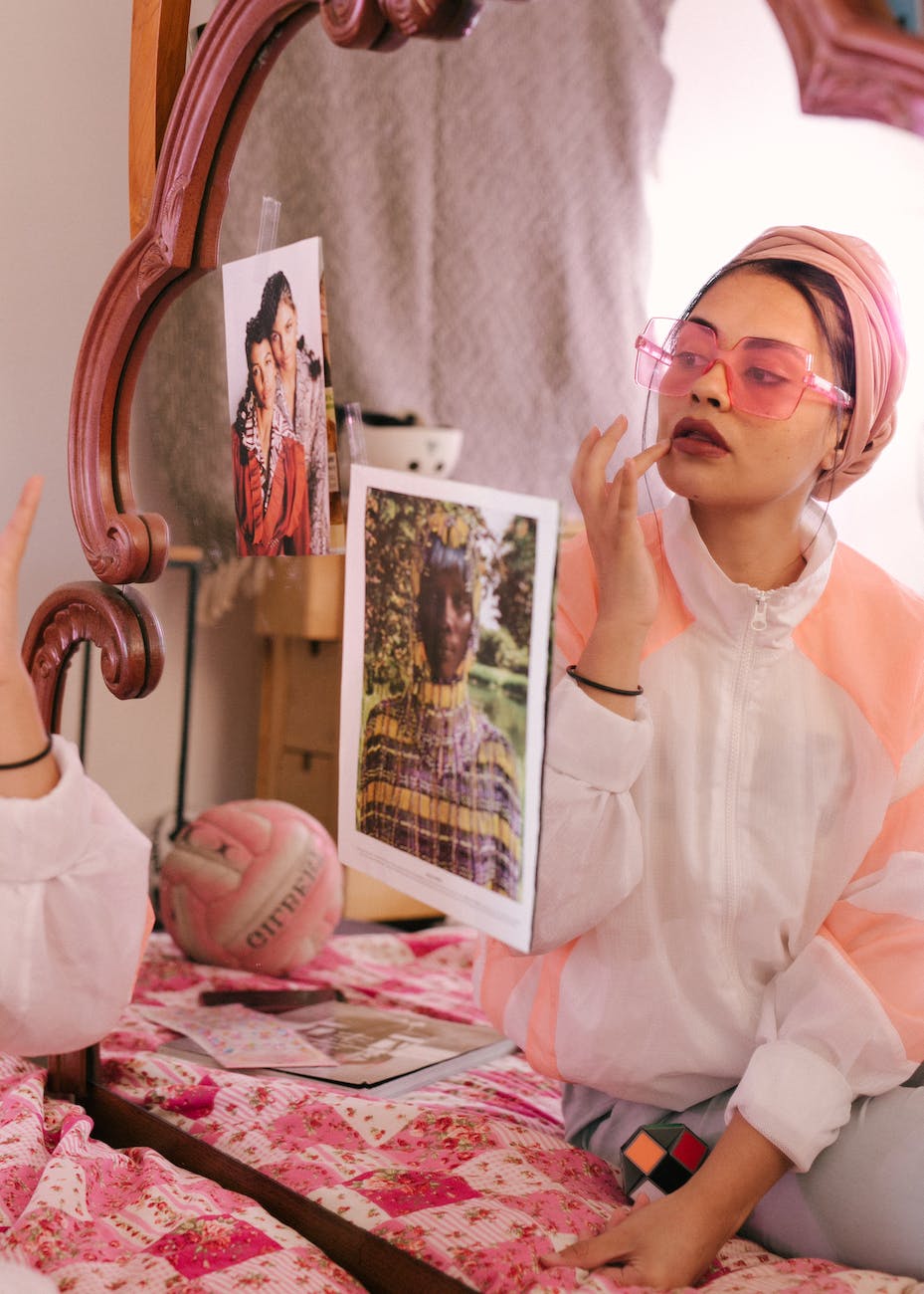 trendy ethnic woman applying lip balm in front of mirror